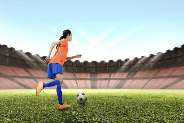 asian female footballer kicking ball 
