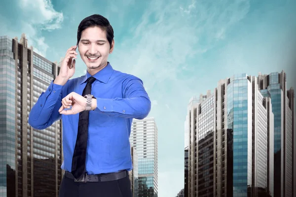 Handsome asian businessman using phone and check the watch with city background