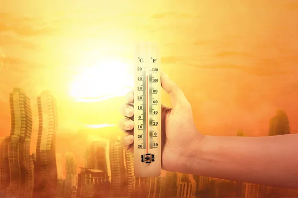 Χέρι κρατώντας θερμόμετρο με υψηλή θερμοκρασία στην πόλη με — Φωτογραφία Αρχείου