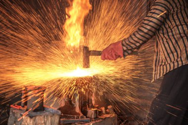 Demirci keris yapmak için erimiş metali çekiçle dövüyor.