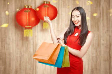 Cheongsam elbiseli Asyalı bir Çinli kadın alışveriş torbaları tutuyor. 