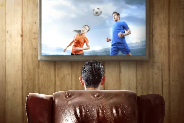 Vista trasera del hombre asiático sentado en el sofá viendo un fútbol — Foto de Stock