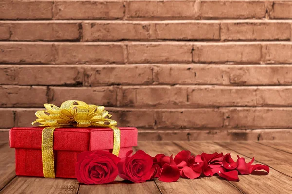 Dárková krabička a červené lístky růží na dřevěném stole — Stock fotografie