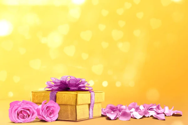 Geschenkdoos en roze rozenblaadjes op een gele achtergrond — Stockfoto