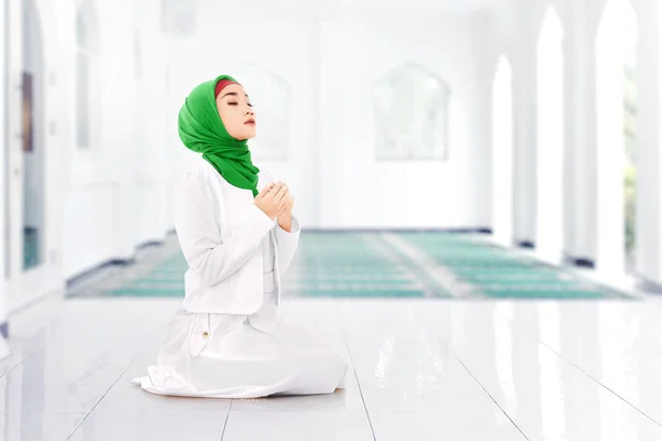 Asian Muslim woman in veil sitting in pray position while raised hands and praying inside the mosque