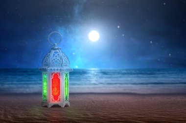 Kumlu sahilde gece manzaralı, renkli ışık saçan Arap lambası.