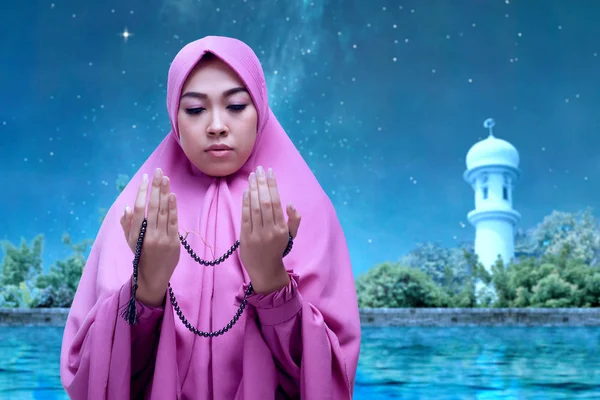 Asian Muslim woman in veil praying with prayer beads on her hands with the night scene background