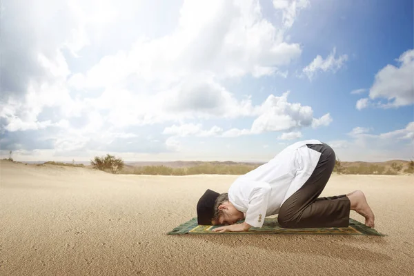Asian Muslim man with a prayer rug in a praying position (salat) on the dune