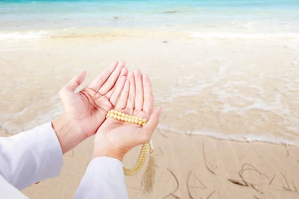 Muslim man praying with prayer beads on his hands on the beach