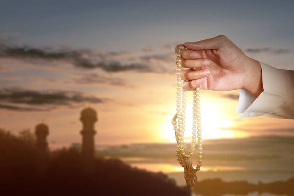 Muslim man praying with prayer beads on his hands with a sunset sky background