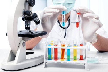 Koruyucu eldivenli doktor elinde mikroskopla koronavirüs kan örneğiyle test tüpleri tutuyor. Grip hastalığını önle Coronavirus