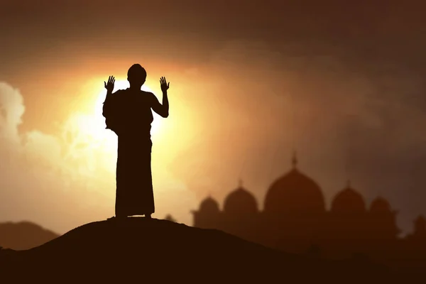 身着伊斯兰长袍的穆斯林男子站在那里祈祷的背影 他举起双臂 背景是夕阳西下的天空 — 图库照片