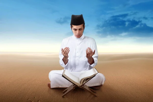 Asian Muslim man sitting while raised hands and praying on the dune