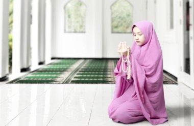 Duvak takmış Asyalı Müslüman bir kadın caminin içinde elinde boncuklarla dua ediyor.