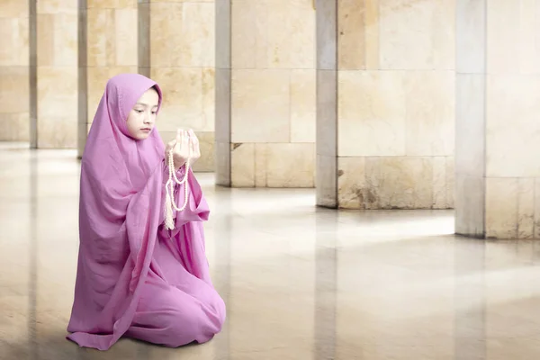 Asian Muslim woman in veil sitting and praying with prayer beads on her hands inside the mosque