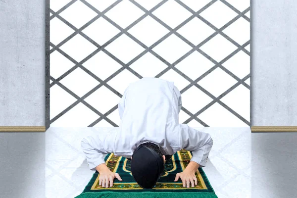 Asian Muslim man with a prayer rug in a praying position (salat) inside the mosque