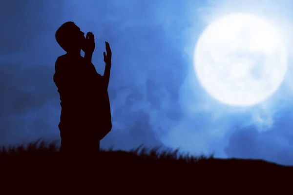 夜の風景を背景に腕を上げながら立って祈るイスラム教徒の男のシルエット — ストック写真