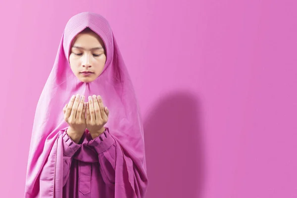 手を上げてピンクの背景で祈りながらベールの中に立つアジア系ムスリム女性 — ストック写真