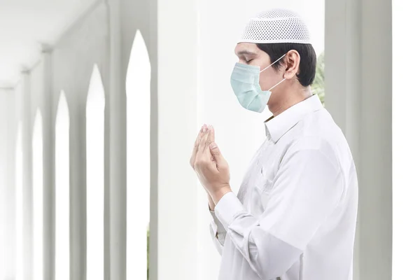 Asian Muslim man wearing flu mask standing while raised hands and praying. Prevent the spread flu disease Coronavirus
