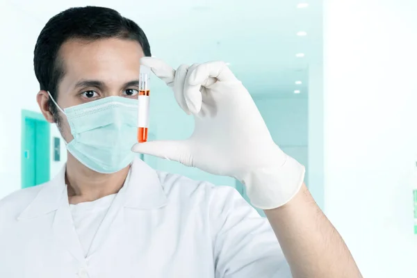 Asian doctor man in flu mask and protective gloves holding a test tube with a blood sample in the hospital