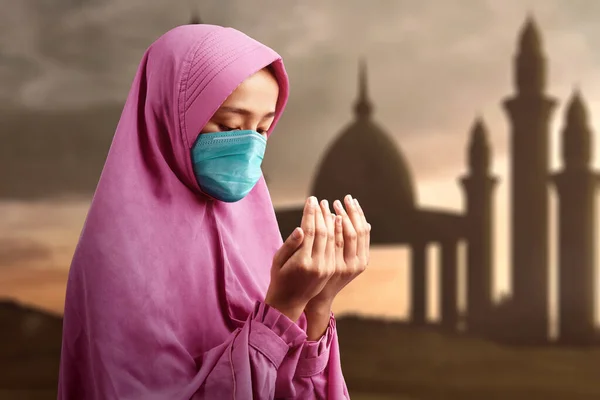 Asian Muslim woman in a veil and wearing flu mask standing while raised hands and praying. Prevent the spread flu disease Coronavirus