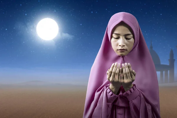 立ち上がる手を上げながらベールの中にアジアのイスラム教徒の女性と夜のシーンを背景に祈る — ストック写真