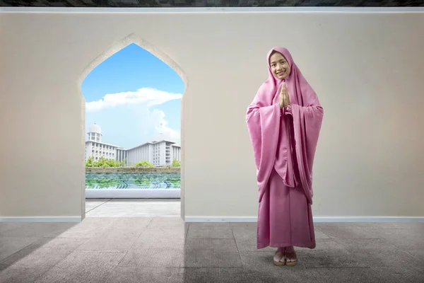 Asian Muslim woman in veil praying with mosque view background