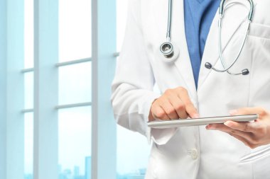 Steteskoplu bir doktor hastanede tablet kullanıyor.