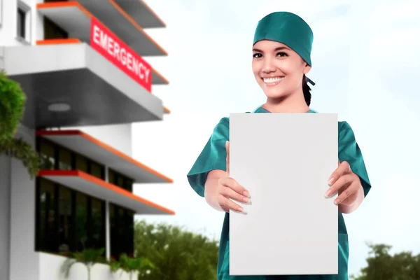 Asian Doctor woman showing blank paper in front of the emergency room in the hospital. Blank paper for copy space