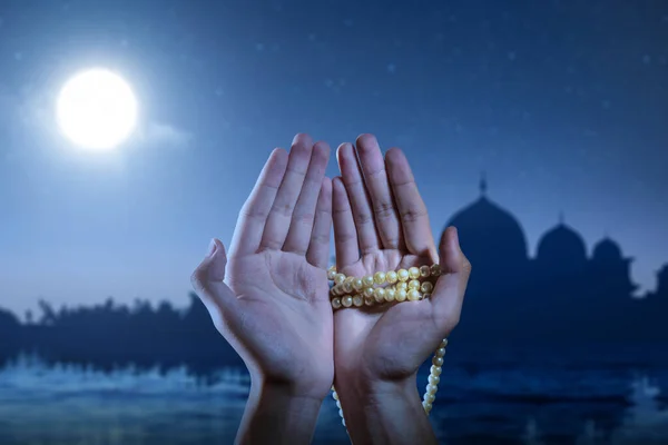 Muslim man praying with prayer beads on his hands with the night scene background