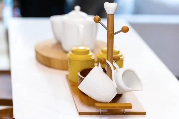 Jars and teapot with wooden rack holder stand for hanging mugs in the kitchen