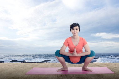 Asyalı hamile kadın yoga yapıyor. Deniz manzaralı yoga minderinde.