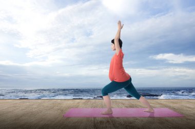 Asyalı hamile kadın yoga yapıyor. Deniz manzaralı yoga minderinde.