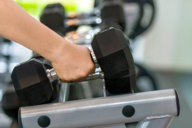 Spor salonundaki bir rafta dambıl tutan bir adam.