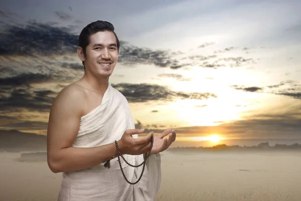 Asian Muslim man in ihram clothes praying with prayer beads on his hands on the dune