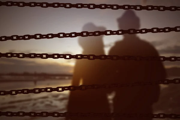 日没時にビーチに立っているカップルとチェーンフェンス 世界難民の日のコンセプト — ストック写真