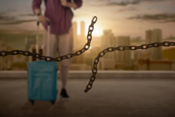 Broken chain with a man with a backpack and suitcase on the city at sunset. World Refugee Day Concept