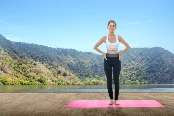 Asian woman is practicing yoga in a yoga mat with lake background
