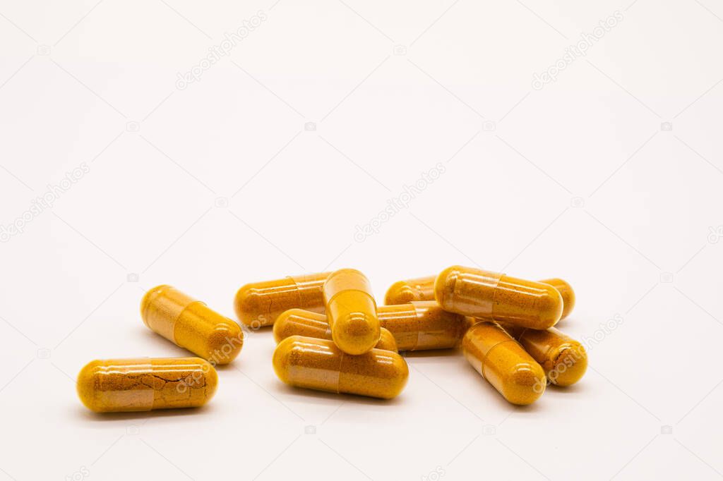 Plastic Capsules containing Turmeric Powder on a white surface and on white background.