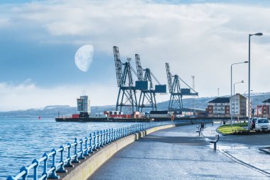 Greenock 'un şehrin batı ucundaki geçidi liman ve ağır vinçleri ile ClydePort Terminali' ne bakıyor. Sabahın köründe Greenock tepelerinde ay ve kar