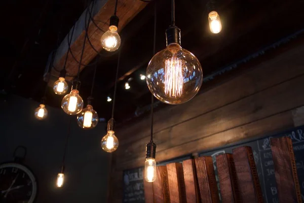 Profundidad superficial de las bombillas eléctricas vintage de campo en primer plano con listones de madera en el fondo en el pub de cerveza occidental de Nueva York con poca luz oscura . — Foto de Stock