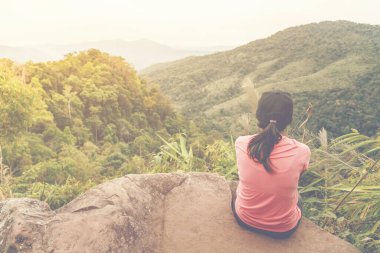 Uçurumda oturan bir kadın ormanın sonundaki yürüyüşten sonra güzel bir manzara görür..