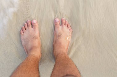 Pürüzsüz deniz dalgalarıyla beyaz kumsalda insan ayakları.