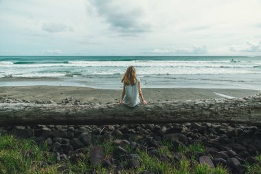 Bir kız bulutlu gökyüzü ve okyanus yüzü olmayan seyir büyük bir tahta bankta oturuyor