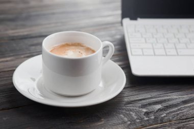 Bilgisayar ve kahve fincanı ahşap masada.