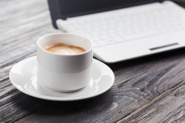 Kahve fincanı yakın up ve arka plan üzerinde koyu ahşap tabl olarak laptop