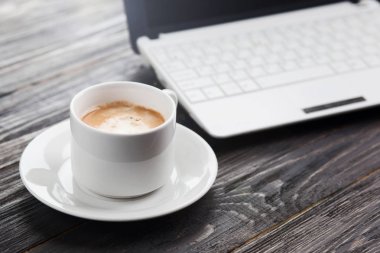 Kahve fincanı ve ahşap masa üzerinde arka plan olarak laptop