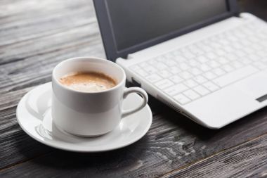 Kahve fincanı ve laptop ahşap masada.