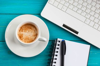 Kahve fincanı, not defteri ve ahşap turkuaz adam üstünde laptop