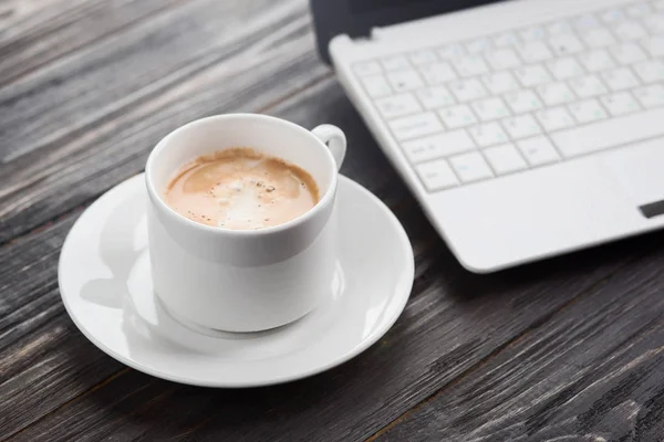 Kahve fincanı yakın up ve ahşap masa üzerinde arka plan olarak laptop